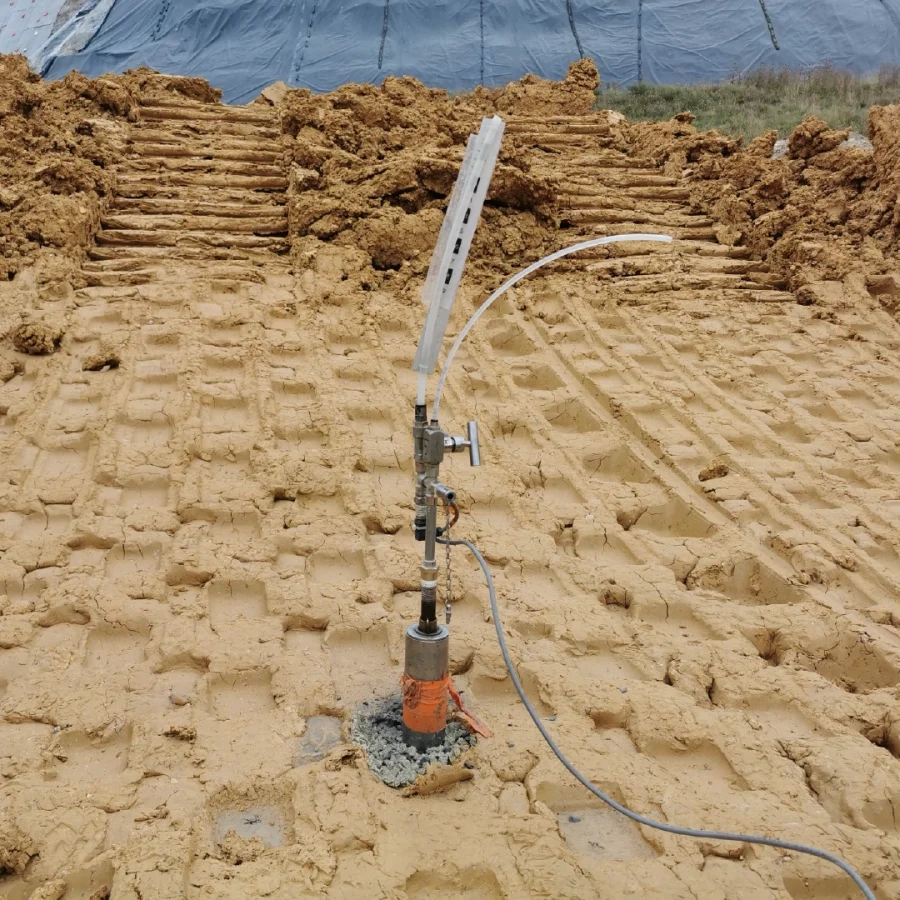 Tête de piézomètre installée dans un sol sableux avec des tuyaux souples, sur un chantier de terrassement.