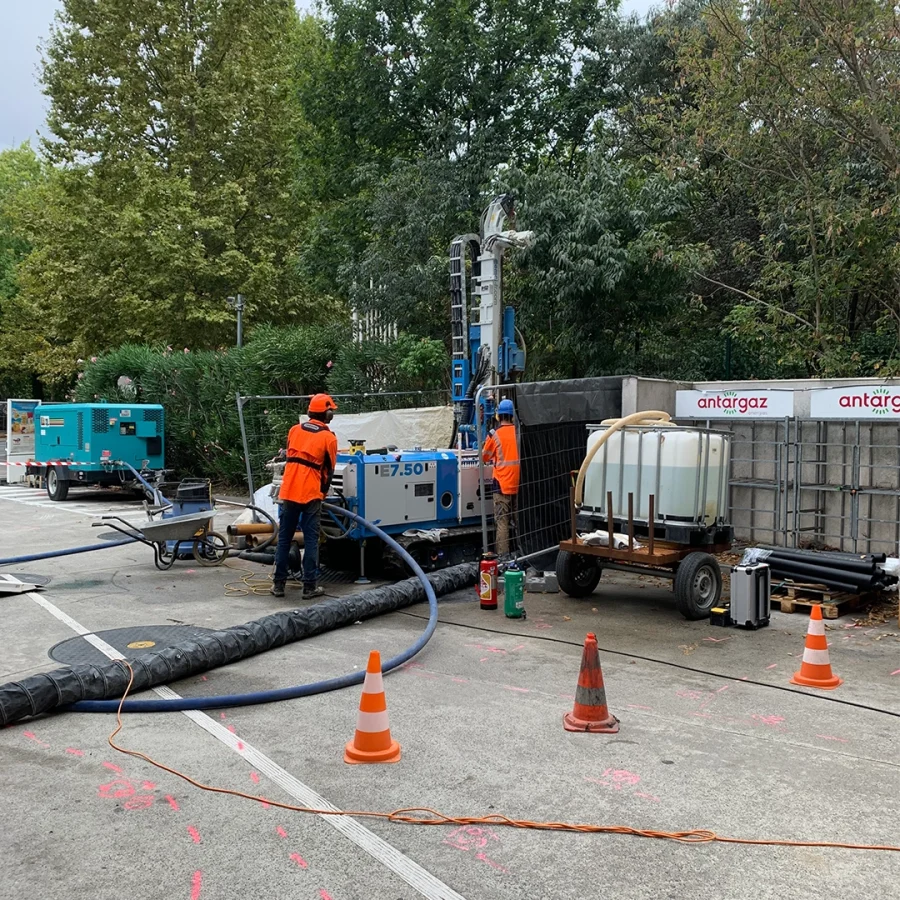 Deux ouvriers en tenue orange travaillant sur une foreuse sur un chantier en milieu urbain