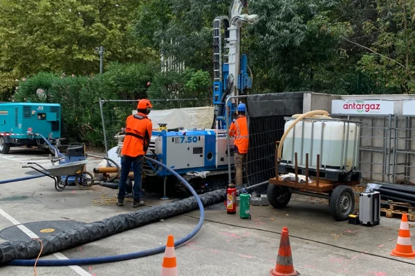 Deux ouvriers en tenue orange travaillant sur une foreuse sur un chantier en milieu urbain